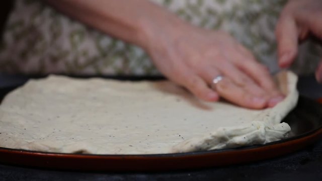 Pressing out raw pizza dough on to a baking pan.
