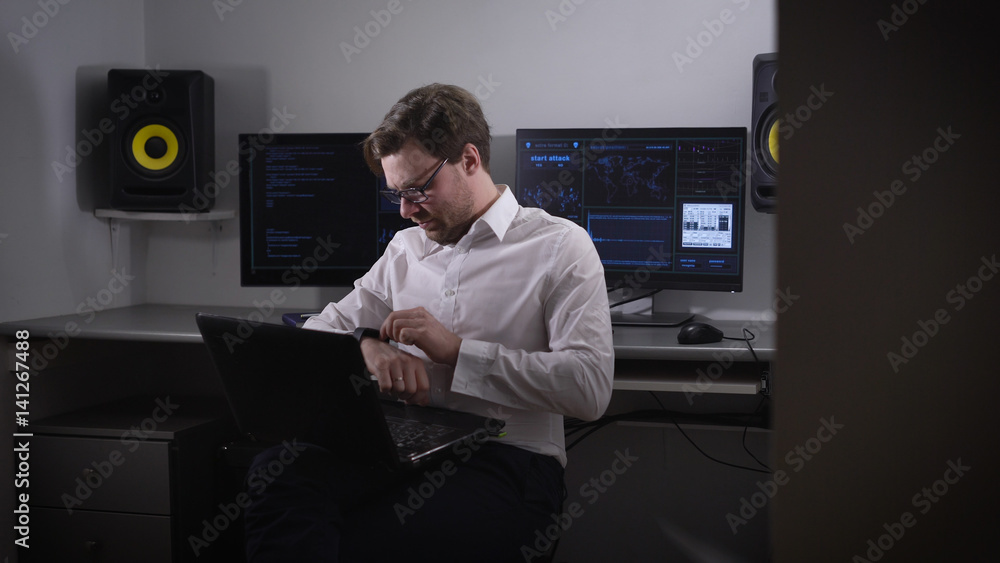 Poster portrait of a young man working on laptop and setting his gadget with smartwatch on his hand. develo