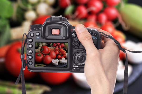 Male hand taking photo of Fresh, raw, organic vegetables on black background with digital DSLR camera. Cooking, Healthy eating concept.