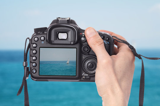 Male hand taking photo of a sailboat on the sea with digital DSLR camera.