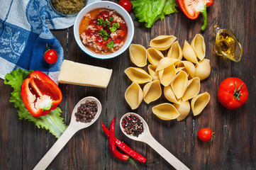 Raw Conchiglioni with minced meat and vegetables on dark wooden background.