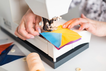 female hands scribbles on the sewing machine geometric color fabric pieces. the process of creating patchwork quilt. the fashion designer's hands at the sewing machine close up. hobby concept.