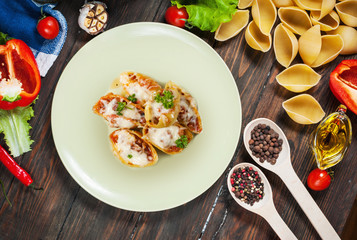 Raw Conchiglioni with minced meat and vegetables on dark wooden background.
