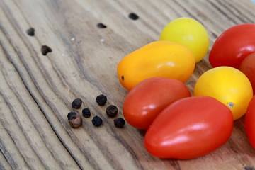 Farbige Tomaten mit schwarzen Pfefferkörnern auf Holztisch