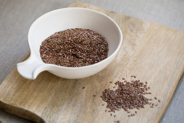 Flax seeds in bowl on wooden board on linen cloth background 