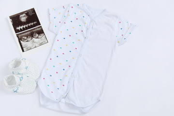 newborn baby set of clothes: patterned bodysuit with knitwear booties and ultrasound on white background with copy space