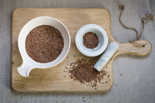 Flax seeds in bowl on wooden board on linen cloth background 