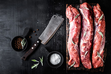 fresh raw pork tenderloin on wooden cutting board on dark background and blank space for your text.