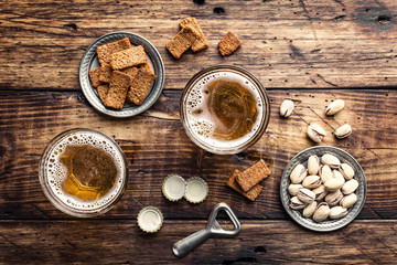 Two glasses of fresh beer and salty snacks on a brown wooden table, top view