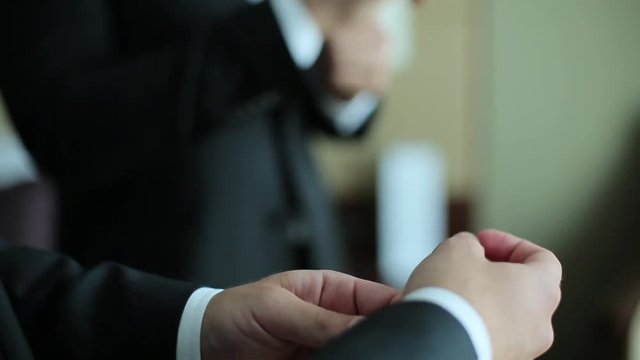 Guy straightens cufflinks on his shirt.