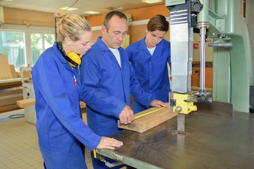 Carpenter measuring wood, being watched by two apprentices