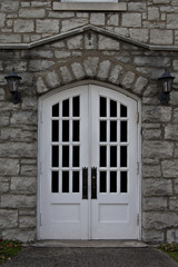 Elegant double, white doors framed with old stone work and a pair of vintage porch lamps.