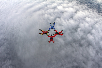 Four skydivers are flying above the clouds.