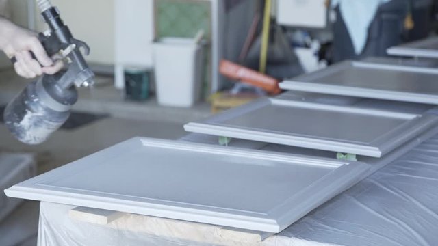 A homeowner handyman type in his garage using a paint sprayer to paint cabinet doors in DIY project.