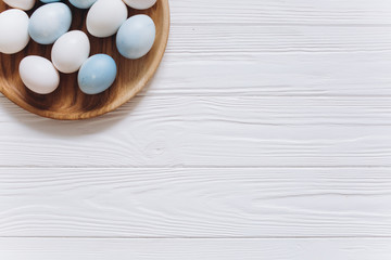 Obraz na płótnie Canvas Pastel colored blue, white and grey Easter eggs in wooden plate on rustic white background.