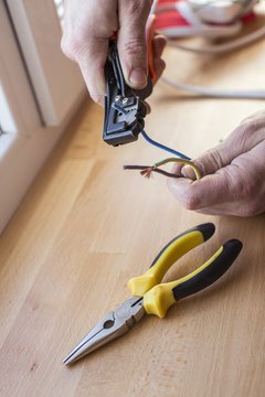Electrician peeling off insulation from wires - closeup on hands and pliers