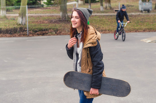 Portrait of of a young happy girl holding a skateboard. Skate park cyclist in the background.