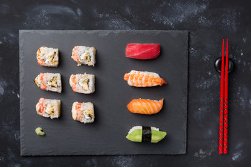 Various sushi and rolls on slate plate and black stone table with chopsticks and wasabi. Japanese cuisine