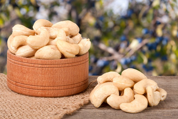 cashew nuts in a wooden bowl on the board with blurred garden background
