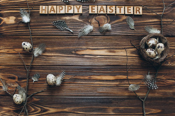 Decoration with quail eggs, nest and feathers. Vintage wooden background with sample text Happy Easter.