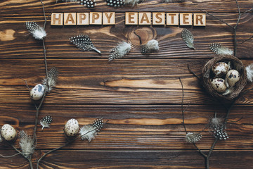 Decoration with quail eggs, nest and feathers. Vintage wooden background with sample text Happy Easter.