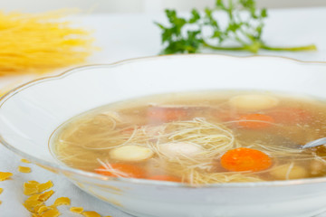 Chicken soup with noodles and vegetables in white plate