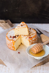 French soft cheese with orange rind on waxed paper, red pepper corns, fork, honey dipper, cut off slice, wood board