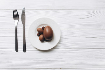 Chocolate easter eggs on plate with knife and fork on white wooden background.