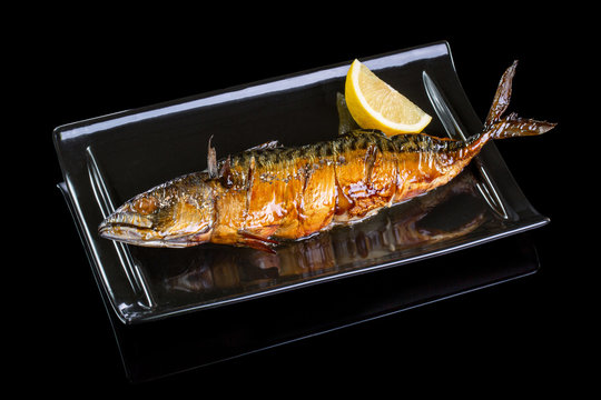 Mackerel cooked in a grill. Served in a black plate, on a black background with reflection.