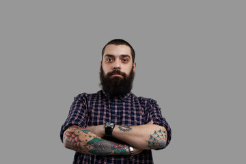 Isolated brutal bearded man with tattooed hands on grey background. Football fun look to the camera. Guy drink a lof of beer and have big stomach. Serious emotion on the face of aggressive person.