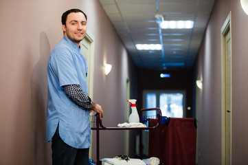 A man who is on the hotel cleaning crew staff is smiling with a towel vacuum in the process of cleaning the hotel rooms and delivering top-knotch service to the guests. - 141292419