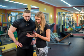 Fit attractive young couple at a gym looking at a tablet-pc as they monitor their progress and...