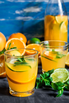 Refreshing beverage, citrus lemonade oranges lime fresh mint in bottle and glasses, sliced fruits on wood table, blue background