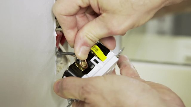 An electrician or homeowner handyman type reattaching the electrical wiring to a ground fault outlet.