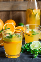 Healthy citrus lemonade from oranges, fresh mint, lime in glasses and bottle on dark stone kitchen table