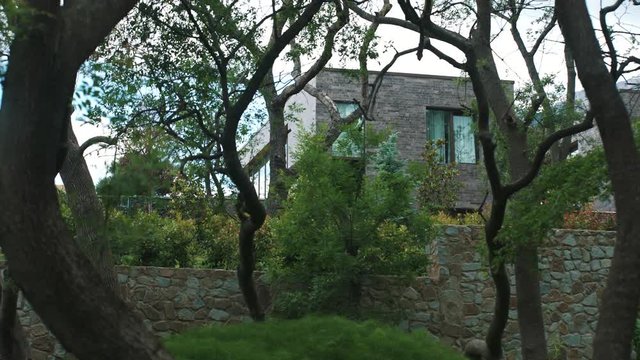 Living resort house with stone siding in forest green leaves and pines, summer time cloudy day, tracking shot