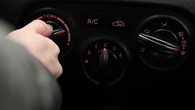 Man twists the knobs of climate control in the car.