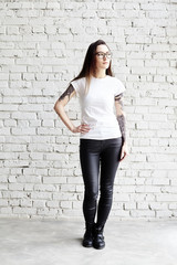 Young tattooed woman wearing blank t-shirt, standing in front of brick wall in loft