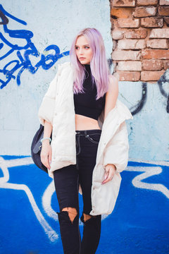 A beautiful girl with purple hair walks the streets of the city. Wearing a jacket, torn jeans