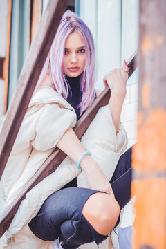 A beautiful girl with purple hair walks the streets of the city. Wearing a jacket, torn jeans