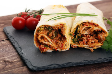Delicious homemade vegetarian couscous wrap with tomatoes, carrots, zucchini, yellow bell pepper and fresh basil on a dark rustic wooden kitchen table