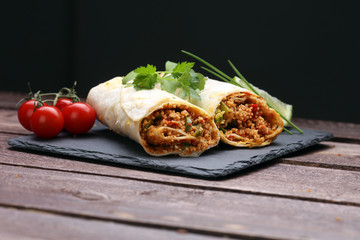 Delicious homemade vegetarian couscous wrap with tomatoes, carrots, zucchini, yellow bell pepper and fresh basil on a dark rustic wooden kitchen table