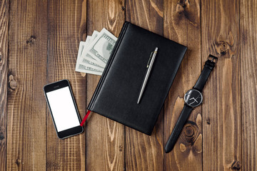 Business Concept - Top view of smartphone, watch, pen, notebook and money on wooden background.