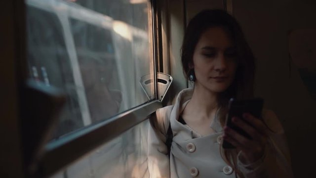 Young woman standing in the train and using smartphone. Attractive girl chatting with friends, browse the Internet.