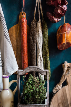 Variety of charcuterie sausages hanging on twine on hooks, wood cutting bard, herbs, linen towel, kitchenware, pantry style