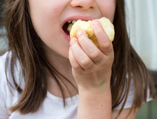 Cropped close up view of little girl eating apple outdoors (selective focus)