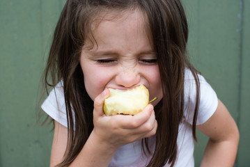 Close up view of little girl taking big bite out of apple (selective focus)
