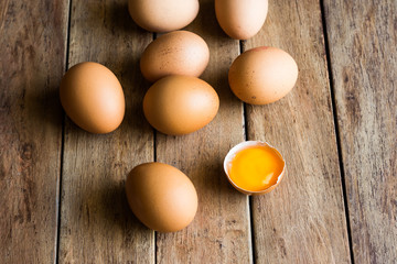 Fresh brown eggs scattered on wood kitchen table, cracked shell with open yolk, soft daylight, top view, Easter, baking concept