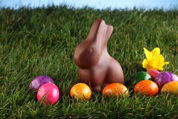 Milk chocolate easter bunny and colorful eggs in fresh green grass - healthy picnic concept