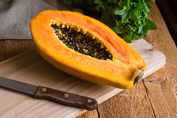 Ripe papaya cut in half on wood cutting board, bunch of fresh mint on rustic kitchen table by window